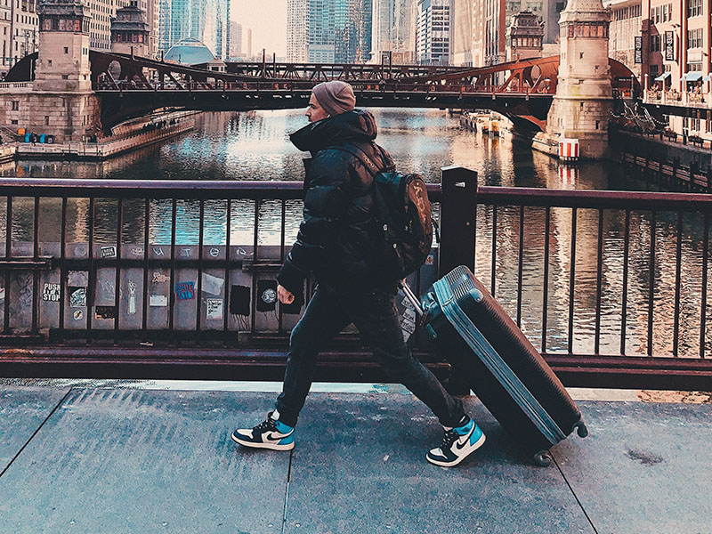 A man walking with a checked suitcase in a large city